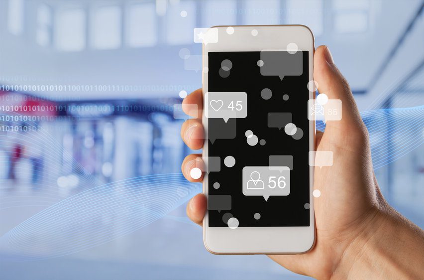 Social media concept. A hand holding a smartphone with social media concepts floating out of the screen.