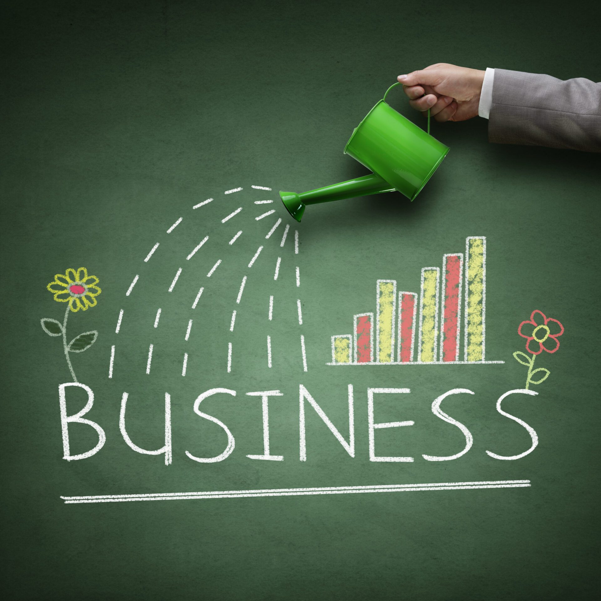 Business growth A green watering can being poured over the word ‘Business’ with flowers and a graph in chalk.
